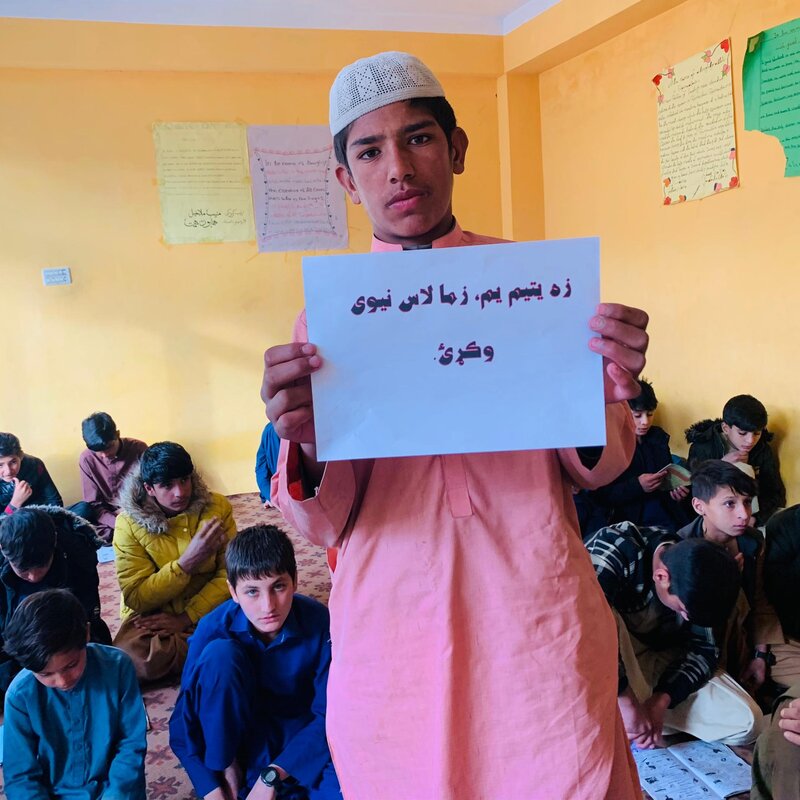 Orphaned student at Zhwand holding a sign about free education